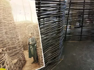 altes Foto eines Soldaten in einem Schützengraben neben einer modernen Installation aus gewundenen Metallstäben