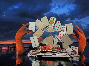 Festspielbühne am See mit riesigen Spielkarten, gehalten von großen Händen, Tänzer auf der Bühne, im Hintergrund Sonnenuntergang und Wasser