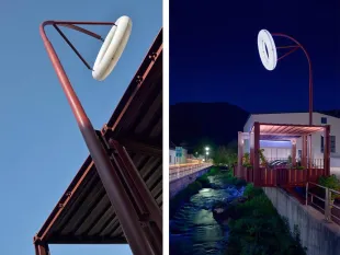 Zwei Ansichten einer modernen Struktur mit einem großen, runden Leuchtenelement an einem roten Gestänge, links bei Tageslicht unter einem Dach, rechts nachts über einem Fluss mit beleuchtetem Gebäude
