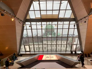 Moderner Raum mit Glasfront und Blick auf eine grüne Kuppel. Podium mit "Politik am Ring", Holzverkleidung, Beleuchtung, wenige Personen.