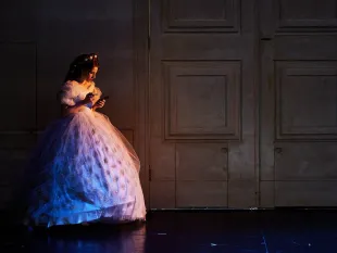 Szene: Kaiserin Sisi in einem funkelnden, weißen Kleid vor einer großen Holztür