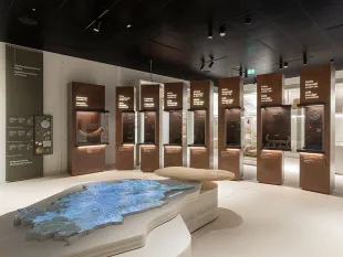 Ausstellungsraum mit beleuchtetem Landschaftsmodell im Vordergrund und mehreren Vitrinen mit historischen Exponaten