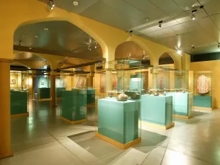 Ausstellungsraum mit orientalischer Architektur, türkise Vitrinen mit Artefakten