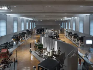 Ausstellungssaal mit historischen Kutschen und Pferdewagen, kunstvoll arrangiert