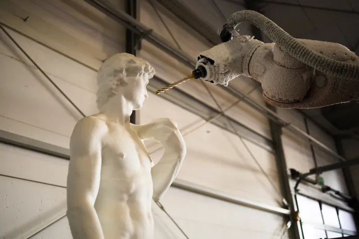 Roboterarm bearbeitet eine Styropor-Statue des David in einer Werkhalle