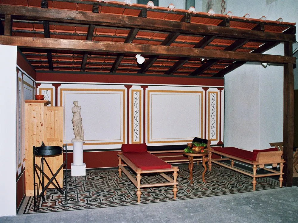 Nachbildung eines römischen Raumes mit Marmorstatue, Liegen mit roten Kissen, Tisch mit Früchten und Mosaikboden unter Holzdach