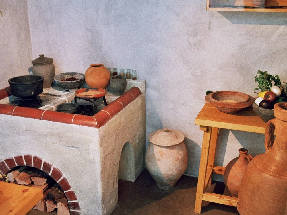 Nachbildung einer historischen Küche mit einem gemauerten Ofen, Töpfen, Krügen und einem Tisch mit Schalen und Lebensmitteln