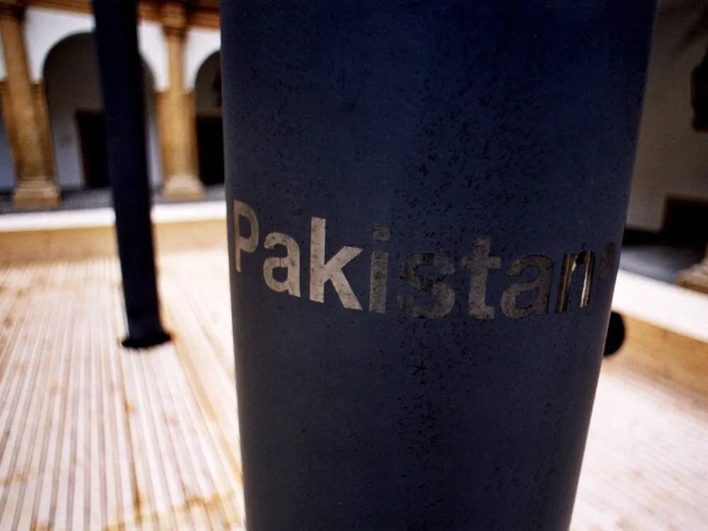 schwarzen Säulen, eine Säule mit der Aufschrift "Pakistan", historische Gebäude mit Bögen im Hintergrund