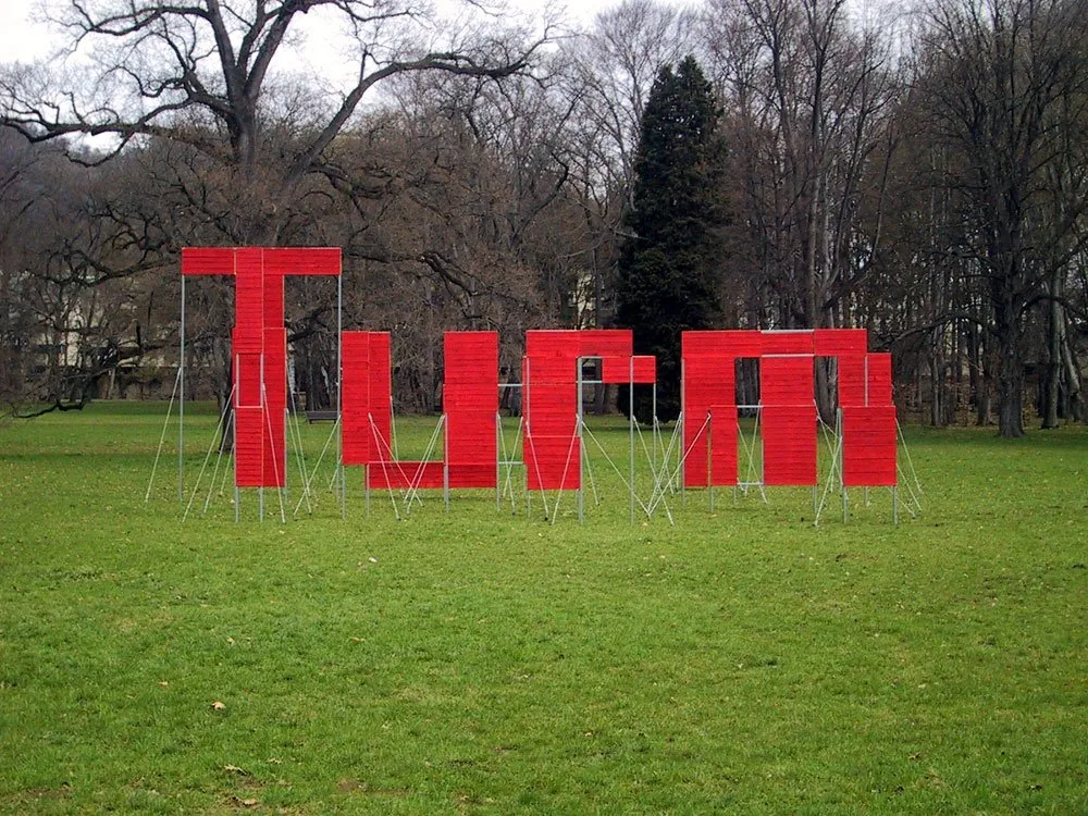 Ausstellungsraum: Grüne Wiese mit roter Installation aus Platten, die das Wort "Turm" bilden
