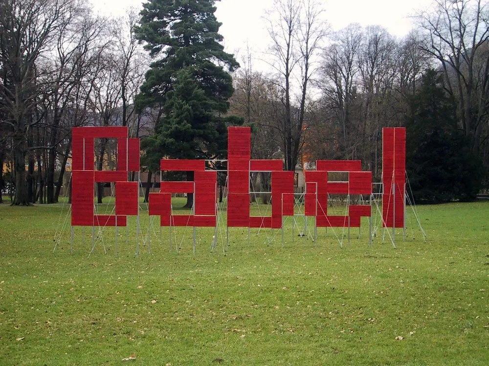 Ausstellungsraum: Grüne Wiese mit roter Installation aus Platten, die das Wort "Babel" bildet
