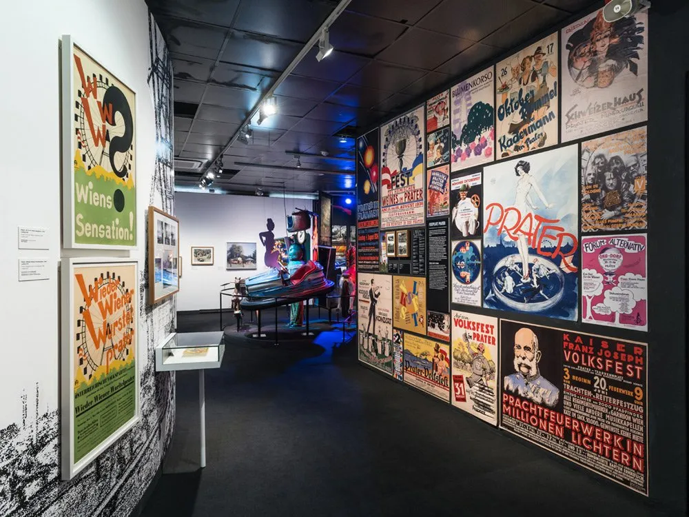 Ausstellungsraum: Viele bunte Poster an den Wänden, Ausstellungsstücke auf Plattformen