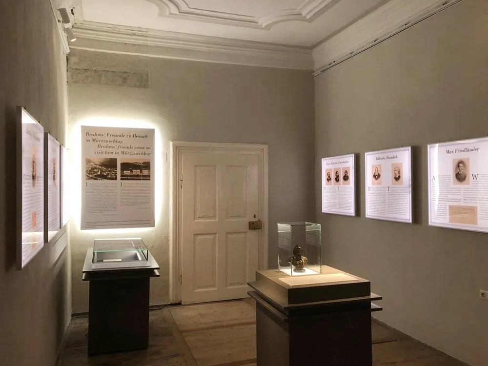 Ausstellungsraum: Beleuchtete Infotafeln mit "Brahms' Freunde zu Besuch in Mürzzuschlag" und Vitrinen mit Artefakten