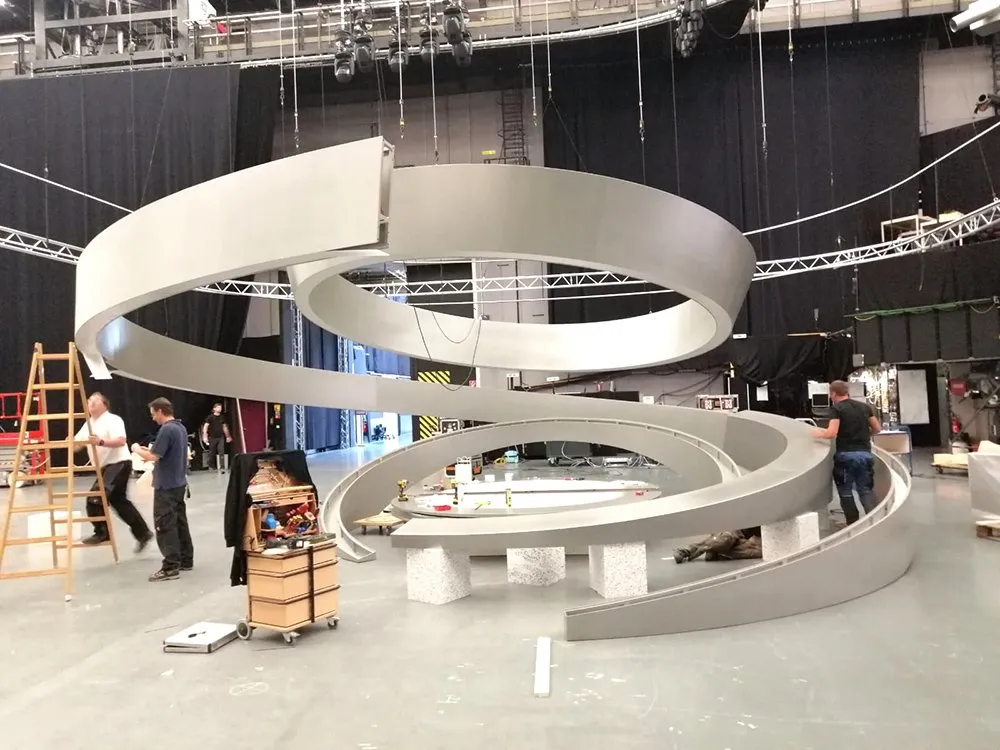 Arbeiter bauen eine spiralförmige Bühne, umgeben von Studiotechnik, Werkzeugen und Materialien