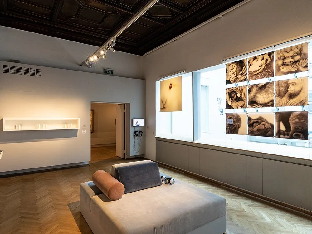Ausstellungsraum: Sitzgelegenheiten, Kunstwerke an den Wänden, Fernseher und Kopfhörern