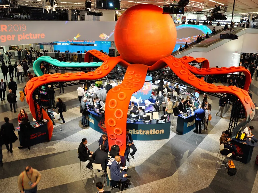 Messehalle mit einer großen Kraken-Installation, umgeben von Registrierungstischen und Besuchern