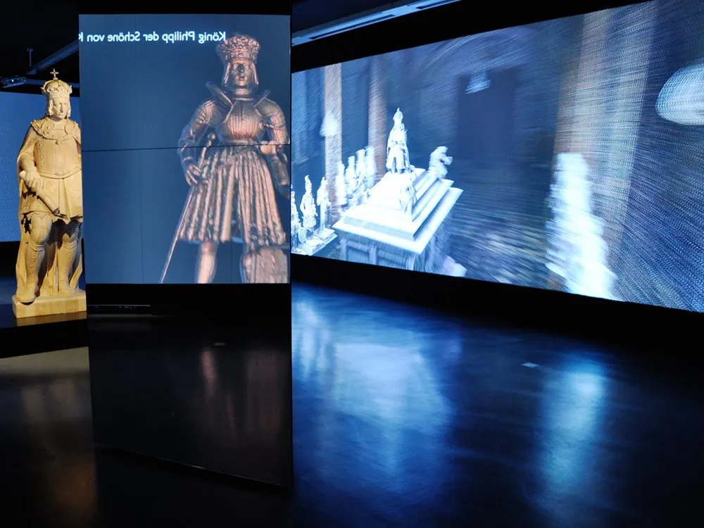 Ausstellungsraum: Große Figur in königlicher Rüstung und Projektion einer historischen Szene mit Statuen und Architektur