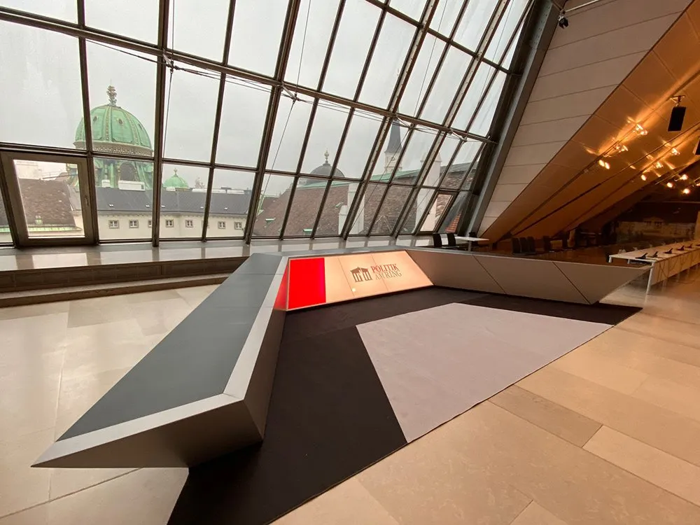 Podium mit Aufschrift "Politik am Ring", ausgestattet mit einer schwarzen und grauen Fläche sowie roter Beleuchtung.