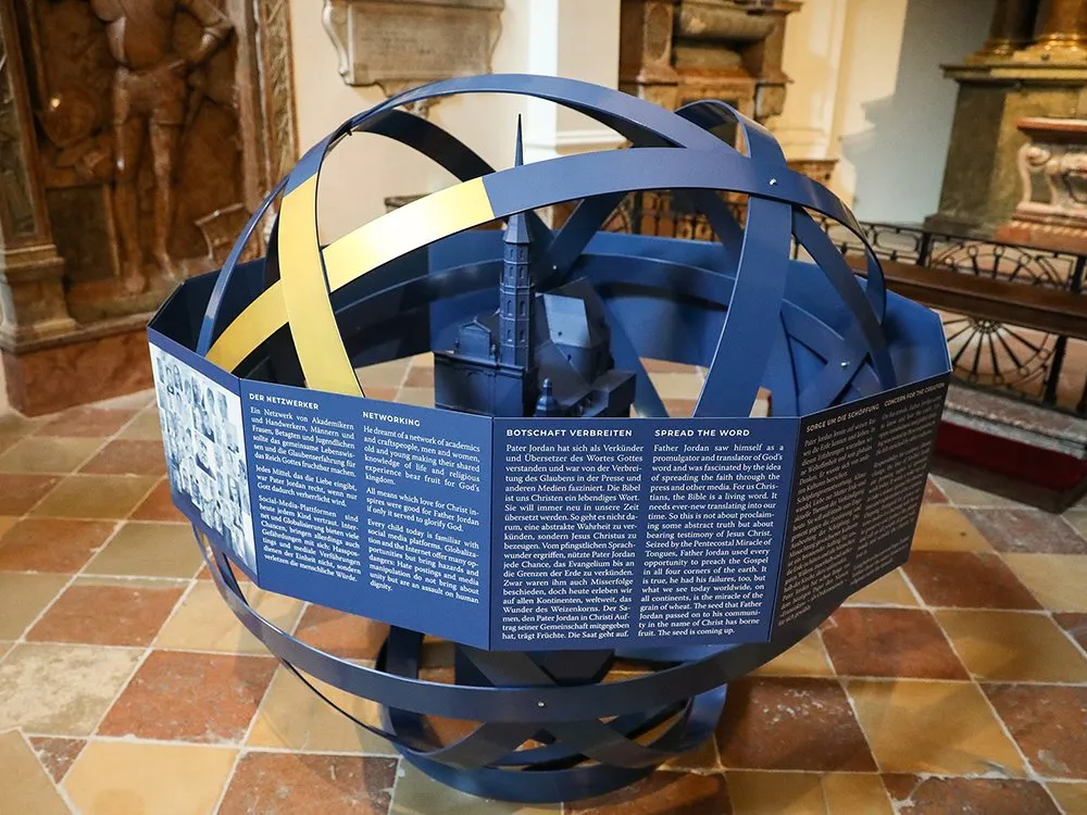 Modell der Michaelerkirche in einem blauen Gestell mit goldenen Streifen, umgeben von mehrsprachigen Informationspaneelen zur 800-jährigen Baugeschichte