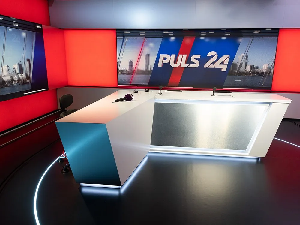 Seitliche Ansicht auf das Pult mit Bildschirmen an der Wand