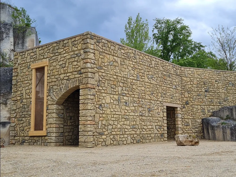 steinernes Gebäude mit einer Fensteröffnung und einem bogenförmigen Eingang in der Naturkulisse des Römersteinbruchs