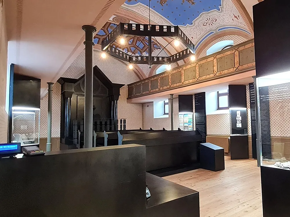 Ausstellungsraum: schwarzer Altar, bemalter Decke, schwarzem Kronleuchter und Vitrinen