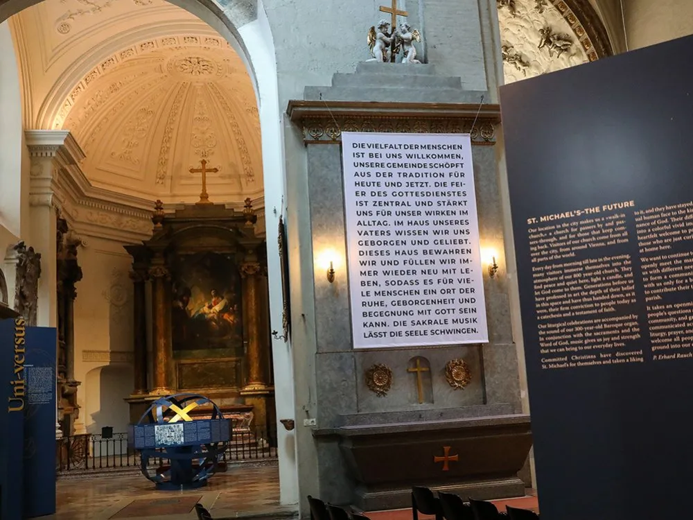 Kirchenraum mit einem Altar und einem Banner mit Text zur 800-jährigen Geschichte der Michaelerkirche, umgeben von Ausstellungstafeln und einem Modell