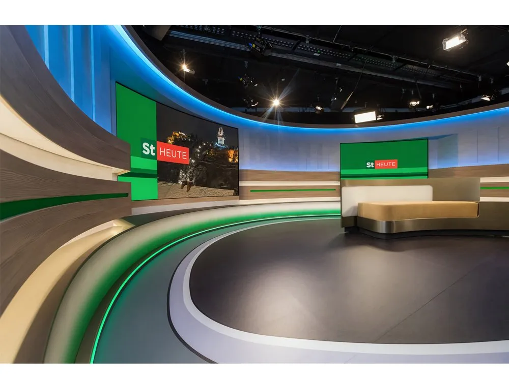 "Steiermark heute"-Studio mit gebogener Bühne, LED-Wänden mit Stadtansichten, grünen Akzenten und einem zentralen Pult