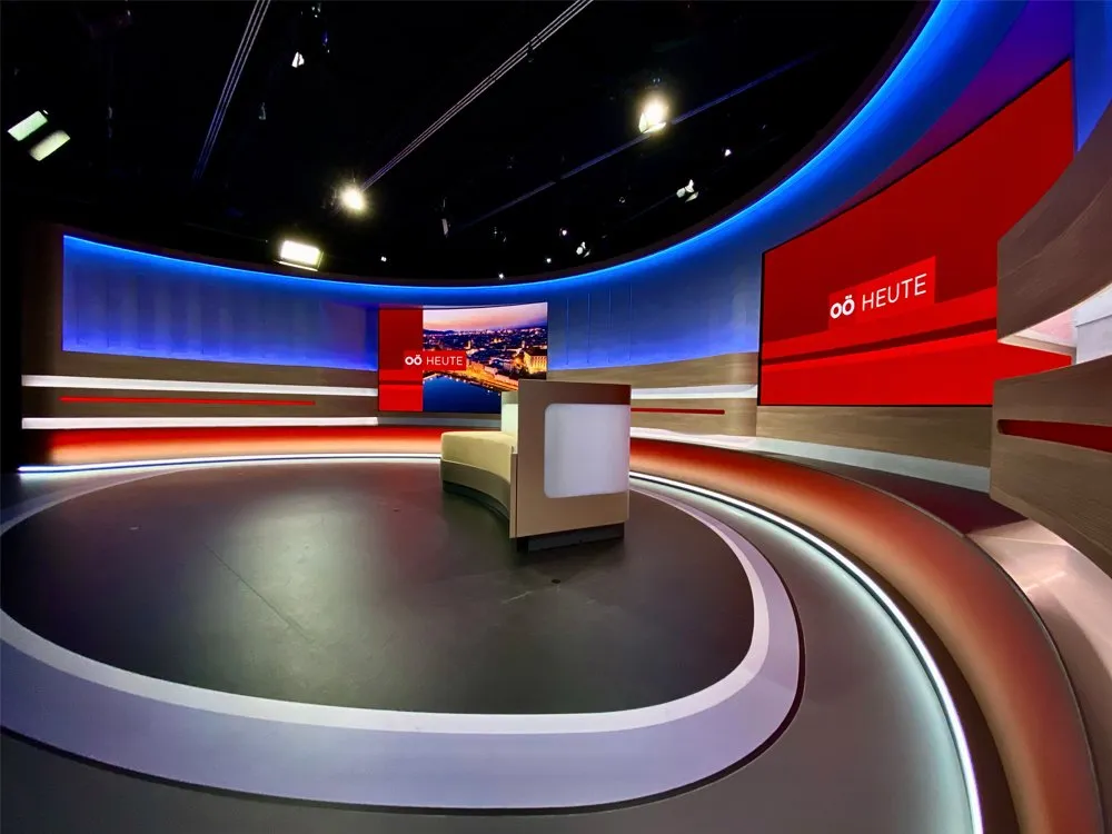"Oberösterreich heute"-Studio mit gebogener Bühne, LED-Wänden mit Stadtansichten, roten Akzenten und einem zentralen Pult