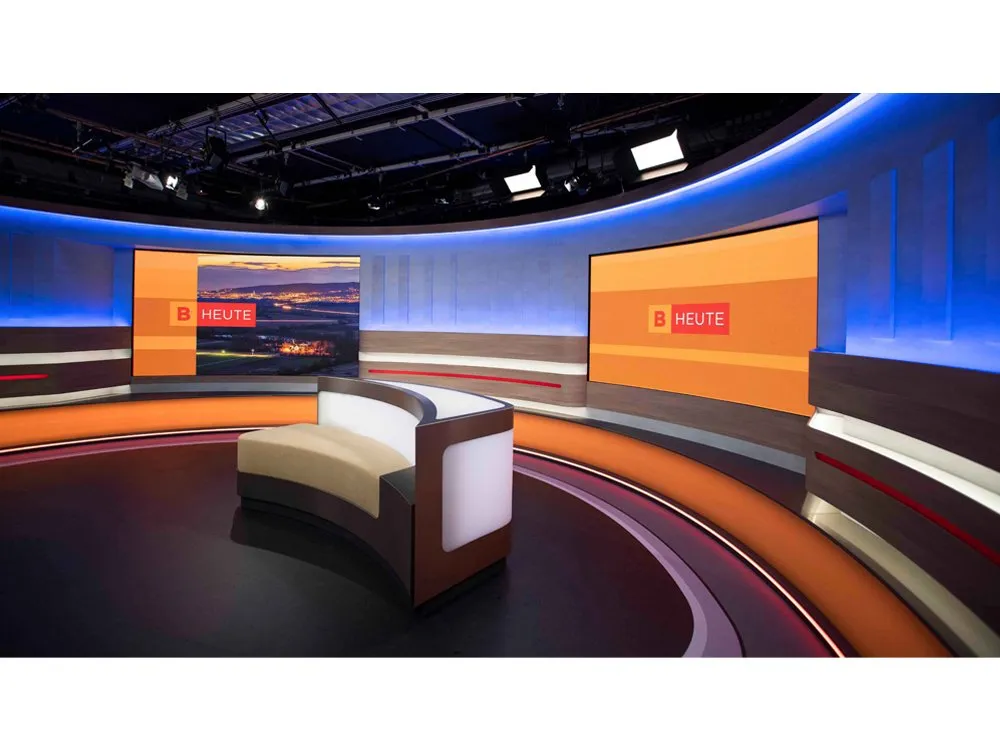 "Burgenland heute"-Studio mit gebogener Bühne, LED-Wänden mit Landschaftsbildern, orangefarbenen Akzenten und einem zentralen Pult