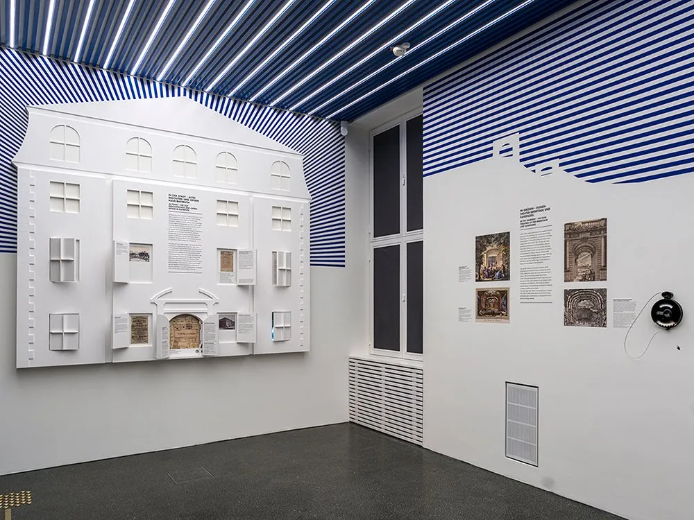 Ausstellungsraum mit einem flachen, an der Wand hängenden Modell des alten Opernhauses und einer Wand Bildern.