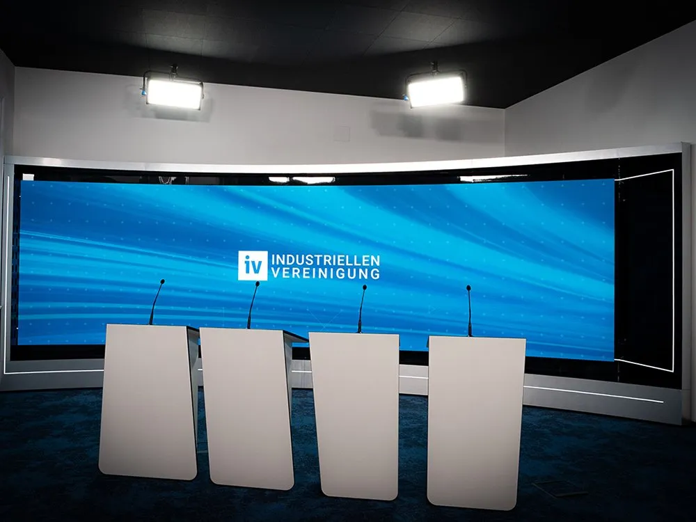 Modernes Studio mit großer LED-Wand im Hintergrund, vier Podiumspulten.