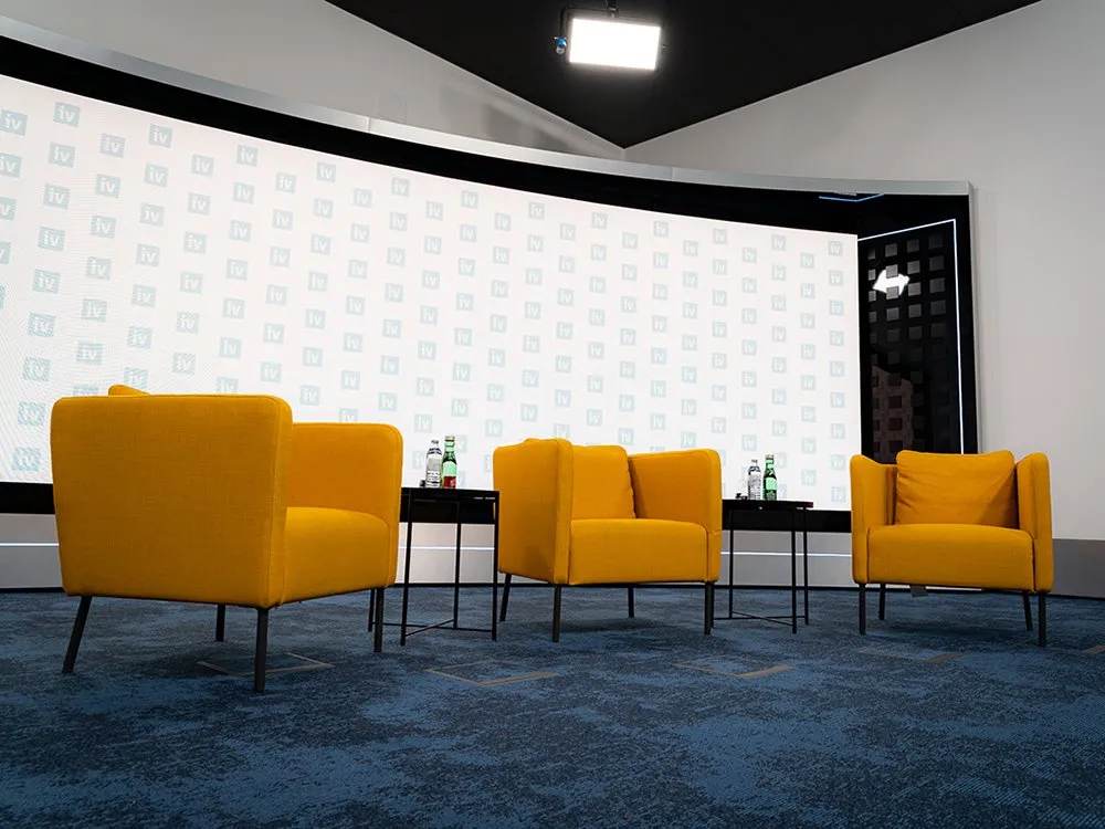 Studio mit drei orangefarbenen Sesseln mit Beistelltischen vor LED-Wand.