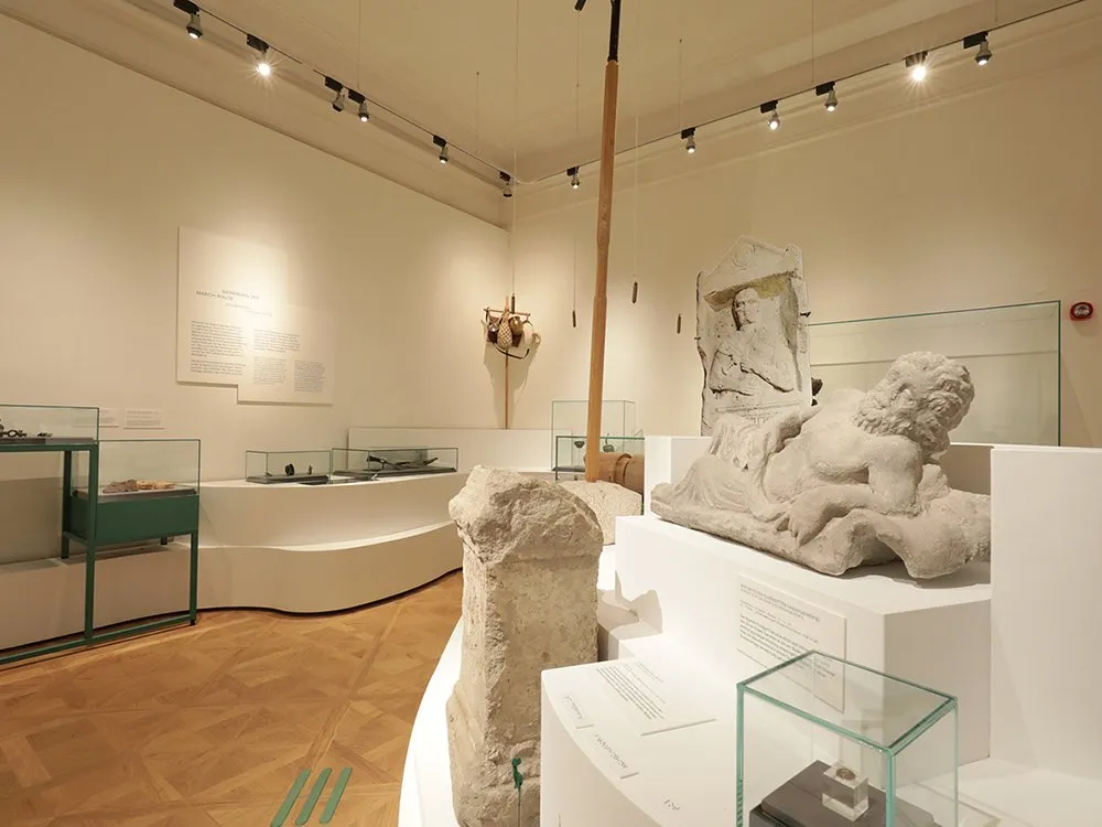 Glasvitrinen und weiße wellenförmige Ausstellungsfläche, die steinerne Skulpturen und Artefakte zeigt