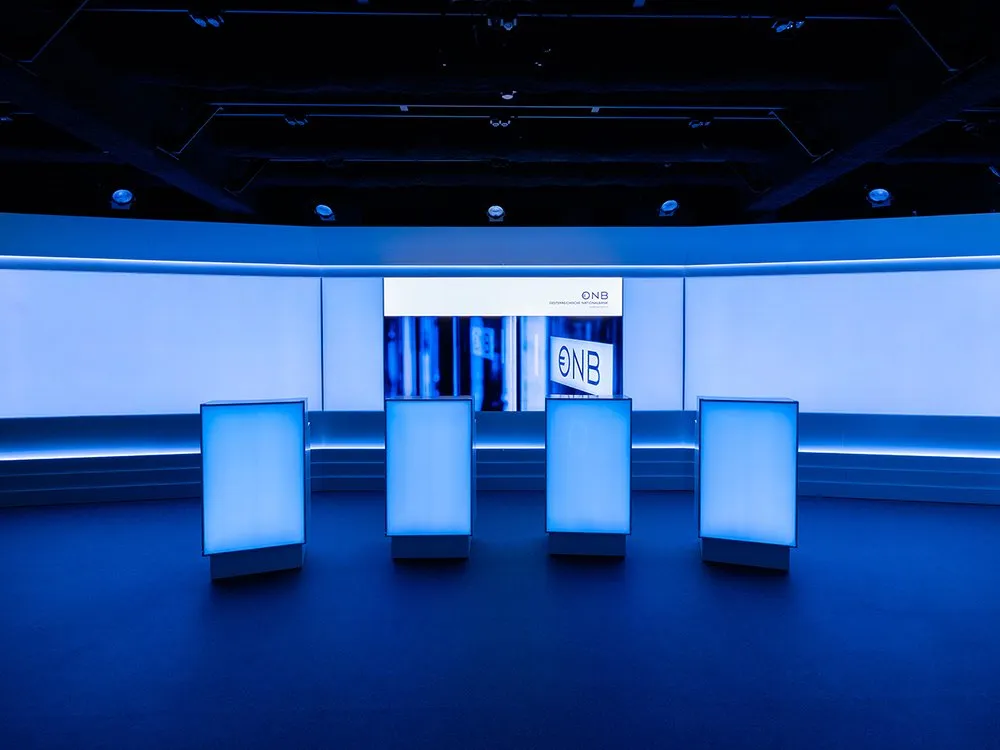 Studio mit vier weißen Pulten und Deckenstrahlern, aus zentraler Perspektive, mit blauer Beleuchtung.
