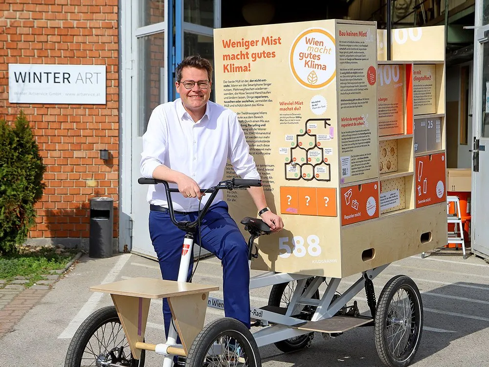 Mann sitzt auf E-Lastenfahrrad mit Holzkiste mit Infografik.