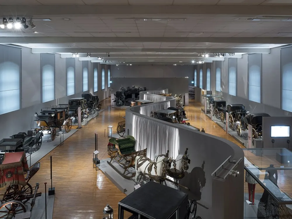 Ausstellungssaal mit historischen Kutschen und Pferdewagen, kunstvoll arrangiert
