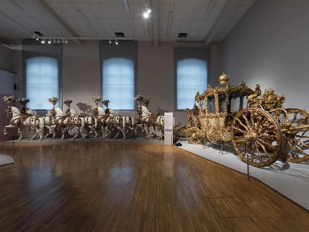 Ausstellungsraum: Prächtige, goldene Kutsche und eine Reihe dekorierter Pferde