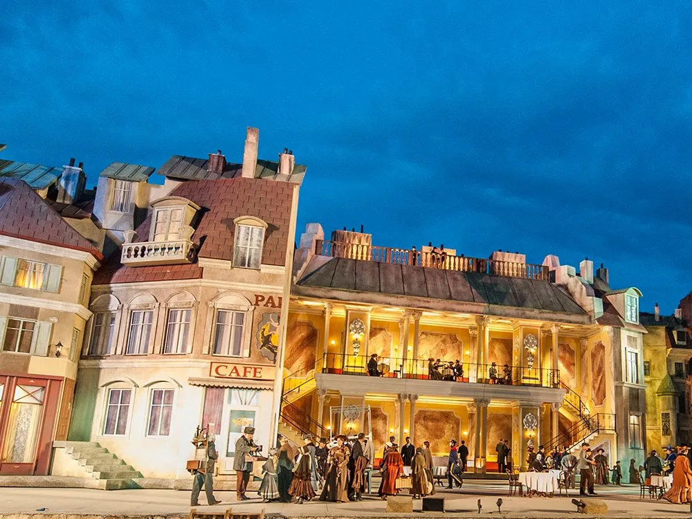 Kulisse eines historischen Pariser Stadtteils mit einem beleuchteten Café und einem Palais, Figuren in historischer Kleidung