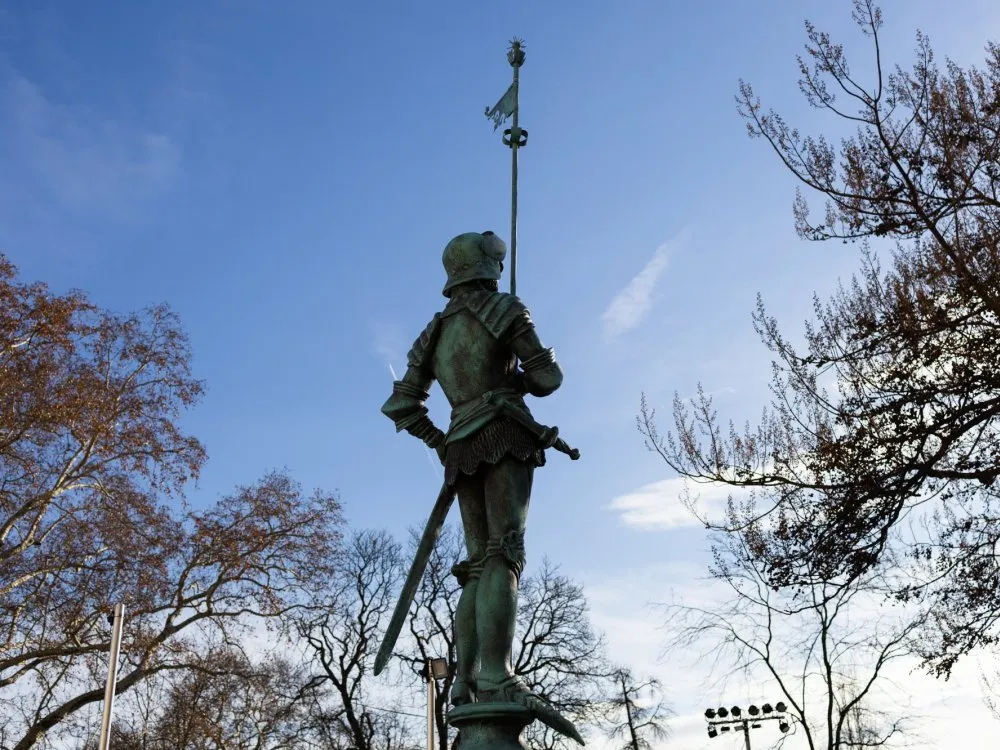 Rückansicht der Statue. Im Hintergrund Bäume.