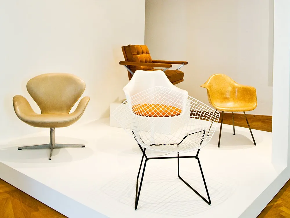 Ausstellung mit vier ikonischen Stühlen in Beige, Orange, Weiß und Gelb auf einem weißen Podest